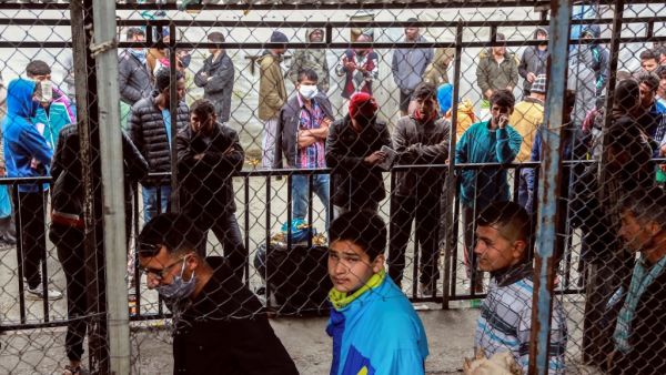 Migrants and refugees, some wearing facemasks for protective measures, queue in a makeshift camp next to the Moria camp on the Greek island of Lesbos on April 2, 2020. Over 20 coronavirus cases were found in a camp near Athens this week. At the camp of Moria on the island of Lesbos, both doctors and migrants say health precautions are not much help in a facility that is so badly overcrowded. The novel coronavirus could spread faster in overcrowded refugee and displaced persons camps than it has anywhere els