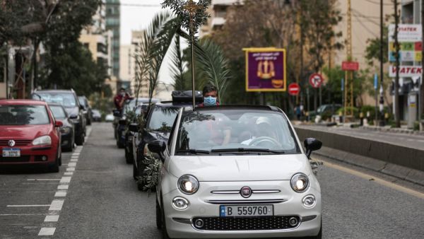 Lebanese Christian boyscouts wearing surgical masks, as a precaution against COVID-19 coronavirus disease, holding palm branches ride in a car procession marking Palm Sunday procession, according to the Western Gregorian calendar, in the capital Beirut on April 5, 2020. PATRICK BAZ / AFP