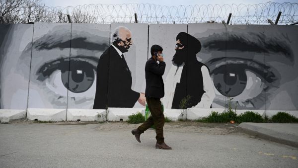 A man wearing a facemask as a precautionary measure against the COVID-19 novel coronavirus walk past a wall painted with images of US Special Representative for Afghanistan Reconciliation Zalmay Khalilzad (L) and Taliban co-founder Mullah Abdul Ghani Baradar (R), in Kabul April 5, 2020. WAKIL KOHSAR / AFP