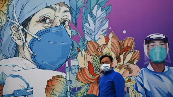 A man wearing a face mask walks in front of a mural at the Leishenshan Hospital that had offered beds for coronavirus patients in Wuhan, in China’s central Hubei province on April 11, 2020. Noel Celis / AFP