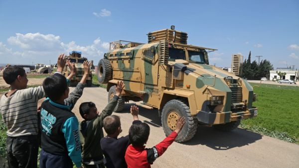 Syrian youths wave to a convoy of Turkish military reinforcements advancing near the town of Hazano in the countryside of Syria's Idlib province, on April 12, 2020, on the highway linking the Bab al-Hawa border crossing with Turkey to Idlib. Aref TAMMAWI / AFP