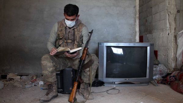 A Turkey-backed Syrian fighter wearing a face mask flips through a book as he rests at a position in the village of Aafes, north of the city of Saraqib in the northwestern Idlib province, during the novel coronavirus pandemic crisis, on April 19, 2020. Abdulaziz KETAZ / AFP