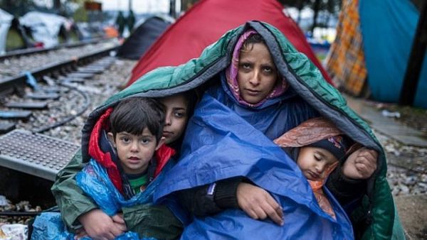 A woman and her children look on as migrants and refugees wait to cross the Greece-Macedonia border in the rain on November 27, 2015 near Gevgelija. (AFP PHOTO / ROBERT ATANASOVSKI)