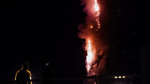 People stand on a bridge and watch a fire that erupts in A 48-Storey Residential Tower in Sharjah on May 5, 2020. AFP