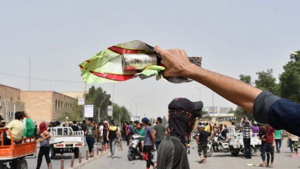 An Iraqi protester holds a smoke grenade fired by security forces amid clashes following an anti-government demonstration in Iraq's southern city of Nasiriyah in Dhi Qar province, on May 10, 2020. Iraq's new government promised to release demonstrators arrested during mass protests that erupted in October and pledged justice and compensation to relatives of over 550 people killed during that unrest. Asaad NIAZI / AFP