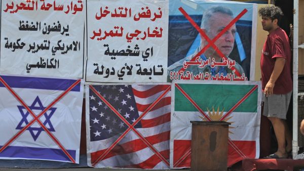 An Iraqi man stands next to the crossed flags of Israel (L), the US and Kurdistan (R) at a protest site along with slogans in Arabic denouncing foreign intervention in Iraq, at Al-Jumhuriyah bridge in the capital Baghdad on May 14, 2020. AHMAD AL-RUBAYE / AFP