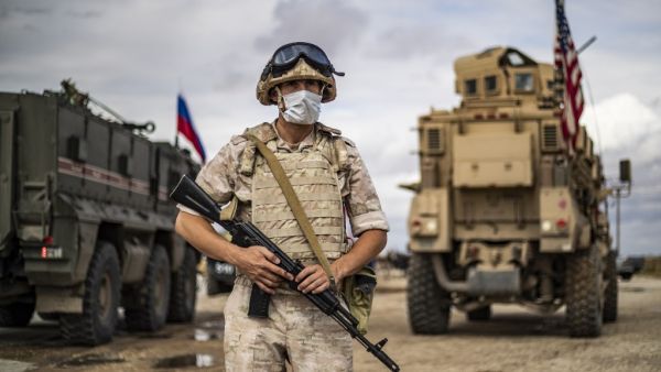 A Russian military police stands next to Russian and US military vehicles along the M4 highway by the town of Tal Tamr on May 25, 2020, as they monitor the reopening of the road to civilian traffic between the border towns of Kobane and Tal Tamr for the first time since a Turkish-backed invasion last year saw the route closed. DELIL SOULEIMAN / AFP