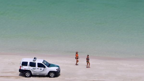 Bathers stare at a police car patroling a public beach at the Jumeirah Beach Residence in the Gulf city of Dubai on May 25, 2020. GIUSEPPE CACACE / AFP