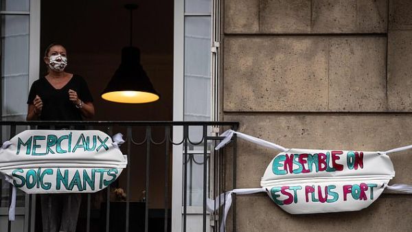 A woman stands on her balcony in Paris behind signs which read 'thank you carers' and 'together we are stronger. (AFP)