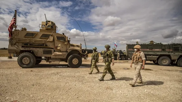 Russian soldiers walk past an US military vehicle along the M4 highway by the town of Tal Tamr on May 25, 2020, as they monitor the reopening of the road to civilian traffic between the border towns of Kobane and Tal Tamr for the first time since a Turkish-backed invasion last year saw the route closed. DELIL SOULEIMAN / AFP