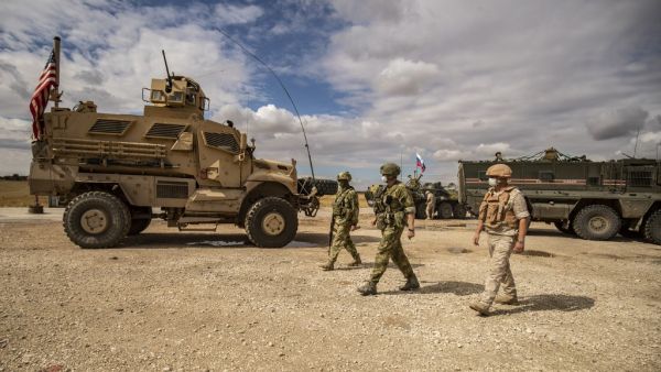 Russian soldiers walk past an US military vehicle along the M4 highway by the town of Tal Tamr on May 25, 2020, as they monitor the reopening of the road to civilian traffic between the border towns of Kobane and Tal Tamr for the first time since a Turkish-backed invasion last year saw the route closed. DELIL SOULEIMAN / AFP