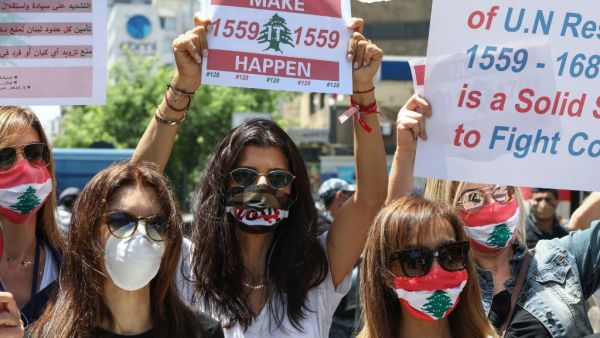 Lebanese anti-government protesters wearing protective gear amid the COVID-19 pandemic lift placards demanding the implementation of United Nations resolutions including the disarmament of armed groups in the country, during a demonstration in the capital Beirut, on May 30, 2020. ANWAR AMRO / AFP