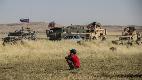 A Syrian boy looks at Russian and US military vehicles in the northeastern Syrian town of al-Malikiyah (Derik) at the border with Turkey, on June 3, 2020. DELIL SOULEIMAN / AFP
