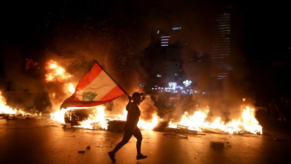 A protester holding the Lebanese flag runs as protesters block the Jounieh Tripoli highway with flaming tires set aflame during a demonstration against dire economic conditions in Jal el Dib North East of the Lebanese capital Beirut late on June 11, 2020. The Lebanese pound sank to a record low on the black market on June 11 despite the authorities' attempts to halt the plunge of the crisis-hit country's currency, money changers said. Lebanon is in the grips of its worst economic turmoil in decades, and hol