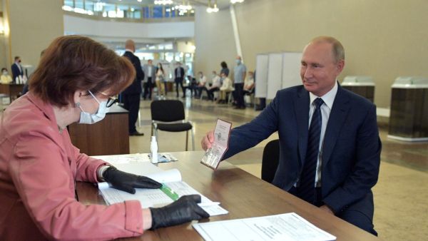Russian President Vladimir Putin shows his passport to a member of a local electoral commission as he arrives to cast his ballot in a nationwide vote on constitutional reforms at a polling station in Moscow on July 1, 2020. Alexey DRUZHININ / SPUTNIK / AFP