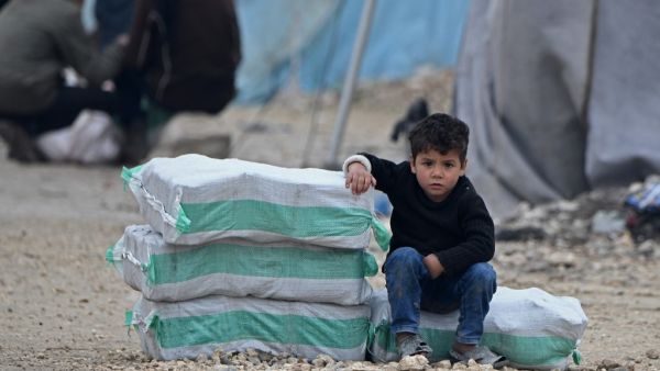 In this file photo a displaced Syrian boy sits next to humanitarian aid, consisting of heating material and drinking water, at a camp in the town of Mehmediye, near the town of Deir al-Ballut along the border with Turkey, on February 21, 2020. Rami al SAYED / AFP