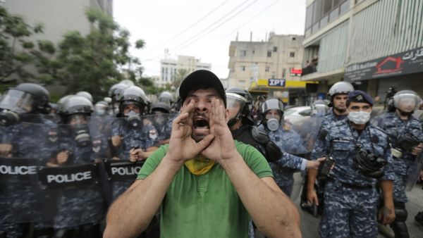 A protester wearing a scarf of the Shiite movement Hezbollah chants slogans while being flanked by Lebanese police during an anti-US demonstration near the United States' Embassy headquarters in Awkar, northeast of the capital Beirut on July 10, 2020. JOSEPH EID / AFP