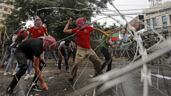 Protesters wearing shirts bearing the logo of the Marxist-Leninist Popular Democratic Party (red) and others wearing bandanas showing the logo of the Shiite movement Hezbollah (yellow) throw stones amidst clashes with security forces during an anti-US demonstration near the United States' Embassy headquarters in Awkar, northeast of Lebanon's capital Beirut on July 10, 2020. JOSEPH EID / AFP