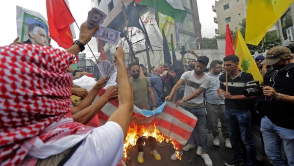 Protesters holding up the flags of the (L to R) Marxist-Leninist Popular Democratic Party, Palestine, and Lebanese Shiite movement Hezbollah burn a make-shift US flag and prints depicting US dollar bills, during an anti-US demonstration near the United States' Embassy headquarters in Awkar, northeast of Lebanon's capital Beirut on July 10, 2020. JOSEPH EID / AFP