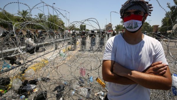 An Iraqi man stands in front of security forces during a protest outside the Green Zone in the capital Baghdad on July 12, 2020 to demand a curb on paramilitary groups and restricting the use of weapons to government security forces. AHMAD AL-RUBAYE / AFP
