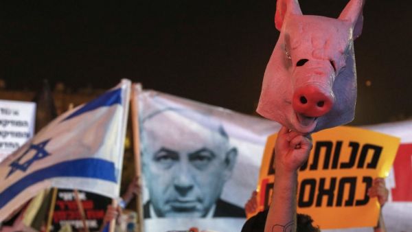 An Israeli protester lifts a mask in the shape of a pig's head during a demonstration in Rabin Square in the central coastal city of Tel Aviv, on July 11, 2020, to protest the government's abandonment of the country's self-employed and other sectors after forcing their businesses to close under COVID-19 regulations, according to the organizers. JACK GUEZ / AFP