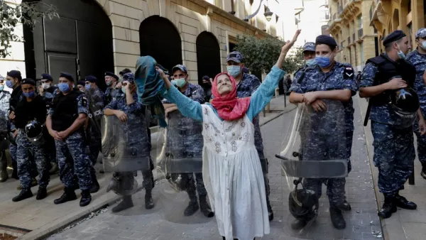 An elderly woman raises her arms in front of Lebanese security forces standing guard in front of the World Bank offices in the downtown district of the Lebanese capital Beirut on July 25, 2020. ANWAR AMRO / AFP