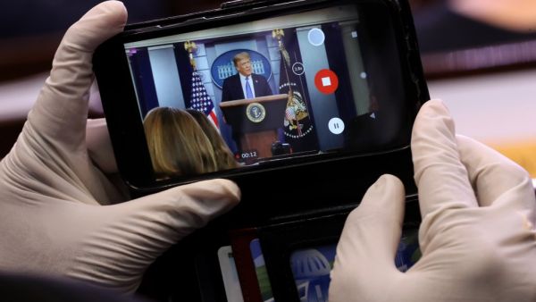 A journalist wears latex gloves to protect against the coronavirus while taking photos of U.S. President Donald Trump during a news conference about his administration's response to the ongoing pandemic in the Brady Press Briefing Room at the White House July 22, 2020 in Washington, DC. This is the second briefing the president has given in as many days. Poll numbers about his handling of COVID-19 have been falling as cases of deadly virus have spiked across the country. Chip Somodevilla/Getty Images/AFP CH