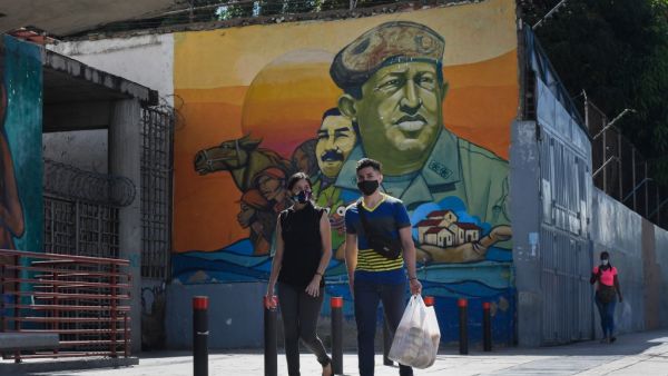People wearing protective masks walks past a mural depicting Venezuela's late President Hugo Chavez, in downtown Caracas on July 28, 2020, after the government intensified a nationwide lockdown as a preventive measure against the spread of COVID-19. Federico PARRA / AFP