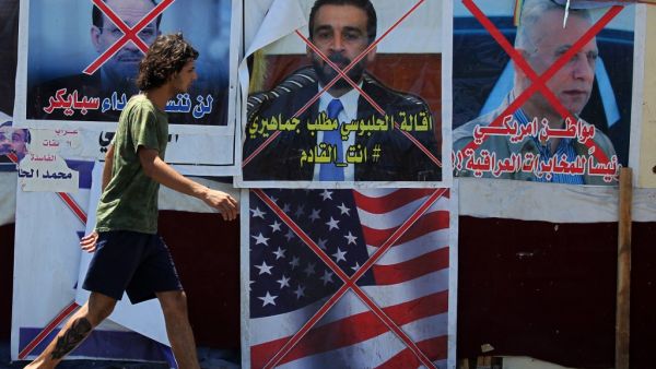 An Iraqi anti-government demonstrator walks past posters of Iraqi polititians and a US flag in Tahrir Square in the capital Baghdad, on August 1, 2020. AHMAD AL-RUBAYE / AFP