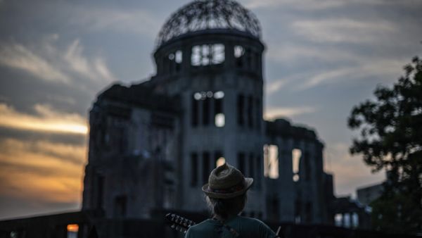 A man plays his guitar in front of in front of ruins of the Hiroshima Prefectural Industrial Promotion Hall, now commonly known as the atomic bomb dome, during sunset in Hiroshima on August 5, 2020. Japan on August 6, 2020 will mark 75 years since the world's first atomic bomb attack, with the COVID-19 coronavirus pandemic forcing a scaling back of annual ceremonies to commemorate the victims. Philip FONG / AFP