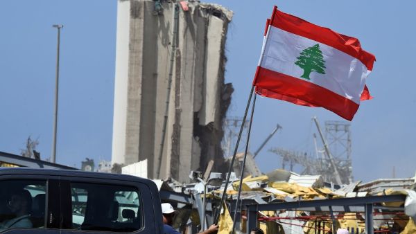 Lebanese people carry the national flag as they drive past the blast site in the capital Beirut on August 8, 2020, four days after a monster explosion killed more than 150 people and disfigured the Lebanese capital. A fire at Beirut port on August 4 ignited a stock of ammonium nitrate and triggered an explosion that was felt in neighbouring countries and destroyed entire neighbourhoods of the city. AFP