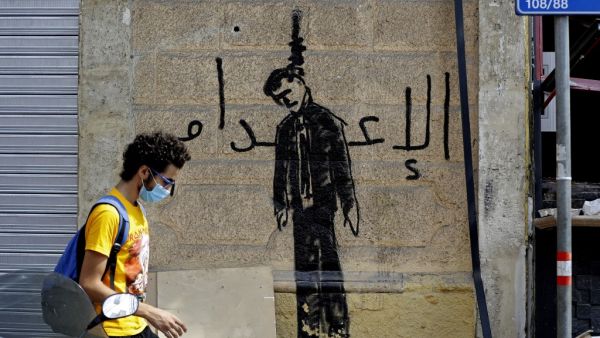 A Lebanese volunteer walks past graffiti depicting a hanged politician with the word "execution", in the devastated Beirut neighbourhood of Gemmayzeh, on August 11, 2020, following a huge chemical explosion that ravaged large parts of the capital. JOSEPH EID / AFP