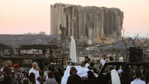 People gather in front of the devastated port of Beirut as a car carrying a statue of the Virgin Mary drives during a procession marking the day of the Assumption on August 15, 2020, more than a week after a massive chemical explosion disfigured the Lebanese capital. STR / AFP