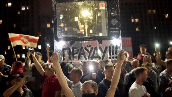 A Belarus opposition supporter holds a fiberglass sheet with a drawn TV and an inscription reading "The truth!!!" near the State TV and radio company during a protest rally against police violence recent rallies of opposition supporters, who accuse strongman Alexander Lukashenko of falsifying the polls in the presidential election, in central Minsk, late on August 15, 2020. Sergei GAPON / AFP