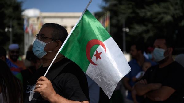 A man wearing a protective mask holds an Algerian flag during a demonstration in front of the United Nations Offices in Geneva against "arbitrary arrests" in Algeria, on August 23, 2020. Fabrice COFFRINI / AFP