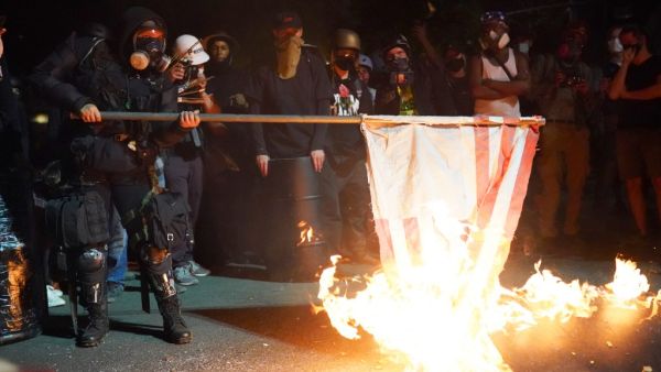 A protester burns an American flag in front of the Mark O. Hatfield U.S. Courthouse in the early morning on August 1, 2020 in Portland, Oregon. Friday was the second night in a row without police intervention, following weeks of clashes between federal officers and protesters in Portland. Nathan Howard/Getty Images/AFP