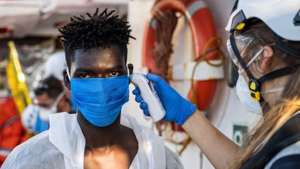 A crew member takes the temperature of a migrant  who has just been helped off Banksy's ship who is wearing protective clothes and a face mask (AFP)