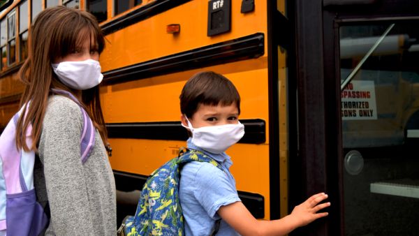 Boy and girl, students, children wearing face masks getting on school bus. (Shutterstock/ File Photo)