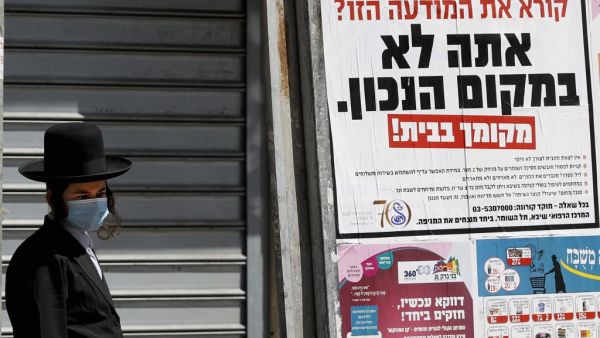 In this file photo taken on April 03, 2020 an ultra-Orthodox Jewish man wearing a mask walks past a sign reading in Hebrew "Reading this ad? You're not in the right place. Your place is at home", in the religious Israeli city of Bnei Brak, near Tel Aviv. (AFP/File Photo)