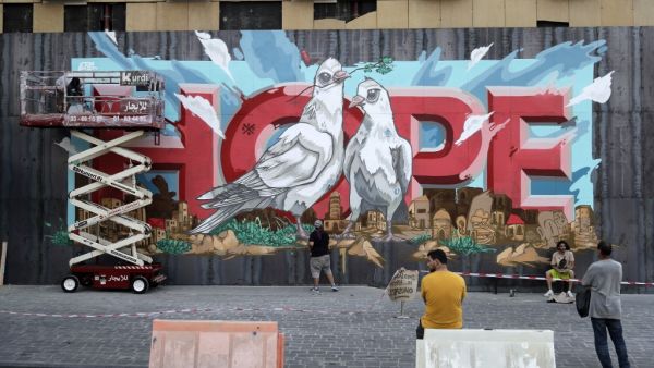 Onlookers watch as artists from the group REK paint a mural on a barrier erected in front of Le Grey hotel in Beirut's downtown district, depicting the city with the word "HOPE" inscribed on it, on September 4, 2020, one month after the August 4 massive blast at the nearby seaport that left scores of people dead or injured ravaged swaths of the Lebanese capital. JOSEPH EID / AFP