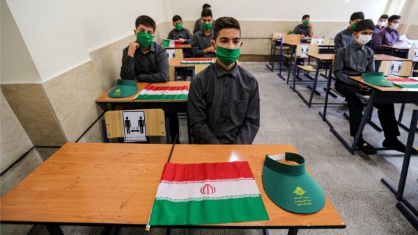 School children sit together in a classroom while mask-clad and distanced apart from each other, new COVID-19 coronavirus pandemic school precautions, with Iranian national flags on the desk of each, on the first day of schools re-opening, at Nojavanan school in the capital Tehran on September 5, 2020. ATTA KENARE / AFP
