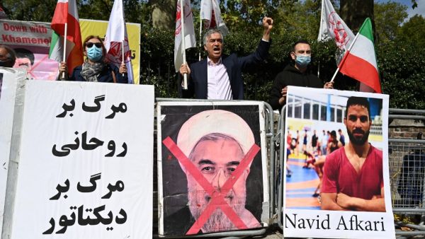 Protesters wave the Lion and Sun flag of the National Council of Resistance of Iran and the white flag of the People's Mujahedin of Iran, two Iranian opposition groups, with a placard depicting the crossed out face of Iran's President Hassan Rouhani as they demonstrate outside the Iranian embassy in London on September 12, 2020 against the execution of Iranian wrestler Navid Afkari in the southern Iranian city of Shiraz and against the Iranian government. Iran said it executed wrestler Navid Afkari, 27, on 