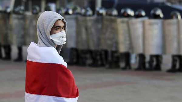 An opposition supporter wrapped in a former white-red-white flag of Belarus stands in front of law enforcement officers blocking the road during a demonstration called by the opposition movement for an end to the regime of authoritarian leader in Minsk on September 20, 2020. Tens of thousands of opposition supporters marched in the Belarusian capital of Minsk defying a heavy security force presence that included water cannons and armoured vehicles. Belarus President Alexander Lukashenko, who has ruled the e