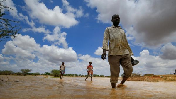 Sudanese people walk in flood water after torrential rain in the town of Osaylat, 50km southeast of Khartoum, on 6 August 2020 (AFP)