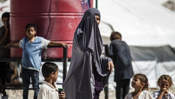 A woman partially covers her face as she stands by children near a water cistern at Camp Roj, housing family members of people accused to belong to the Islamic State (IS) group who were relocated from al-Hol camp, in the countryside near al-Malikiyah (Derik) in Syria's northeastern Hasakah province on September 30, 2020. Delil SOULEIMAN / AFP