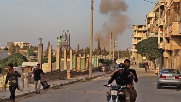A smoke plume rises following an explosion in the town of Ariha in the rebel-held northwestern Idlib province on October 20, 2020, while a Turkish military convoy drives through after vacating the Morek post in Hama's countryside. Turkey started withdrawing from one of its largest outposts in northwest Syria encircled for the past year by Syrian regime forces, a war monitor and a pro-Ankara rebel commander said. The outpost in Morek is Turkey's largest in the northwest province of Hama, which is now mostly 