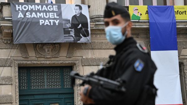 A French police officer stands next to a portrait of French teacher Samuel Paty on display on the facade of the Opera Comedie in Montpellier on October 21, 2020, during a national homage to the teacher who was beheaded for showing cartoons of the Prophet Mohamed in his civics class. France pays tribute on October 21 to a history teacher beheaded for showing cartoons of the Prophet Mohamed in a lesson on free speech, an attack that has shocked the country and prompted a government crackdown on radical Islam.