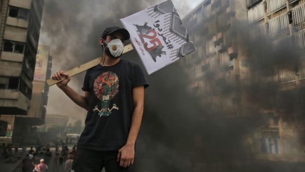 An Iraqi protester carries a placard reading in Arabic "Revolt" during a demonstration on the Sinak bridge in the capital Baghdad on October 25, 2020, marking the first anniversary of a mass anti-government movement. AHMAD AL-RUBAYE / AFP