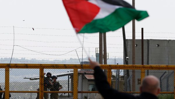 A Palestinian protester waves his national flag in front of Israeli security forces outside the compound of the Israeli-run Ofer prison near Betunia in the Israeli occupied West Bank, March 30, 2016. (AFP Photo)