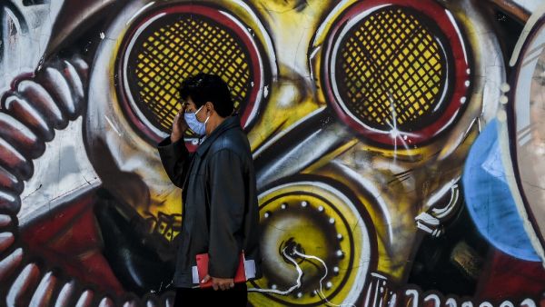 A man wearing a face mask as a preventive measure against the novel coronavirus COVID-19, walks by a graffiti in Bogota on August 25, 2020 Colombia will begin a new phase against the pandemic in September with "specific restrictions" and reactivation of economic sectors given the downward trend in infections,President Ivan Duque announced on August 24. Juan BARRETO / AFP